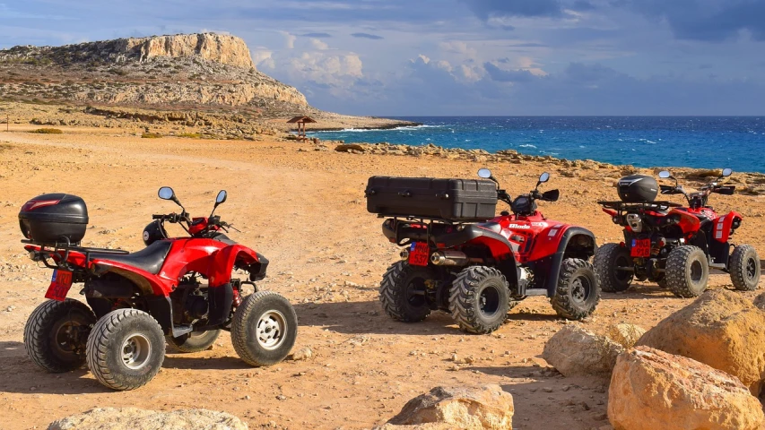 a couple of red four wheelers sitting on top of a sandy beach, a picture, shutterstock, greek setting, panorama, professional work, high quality product image”