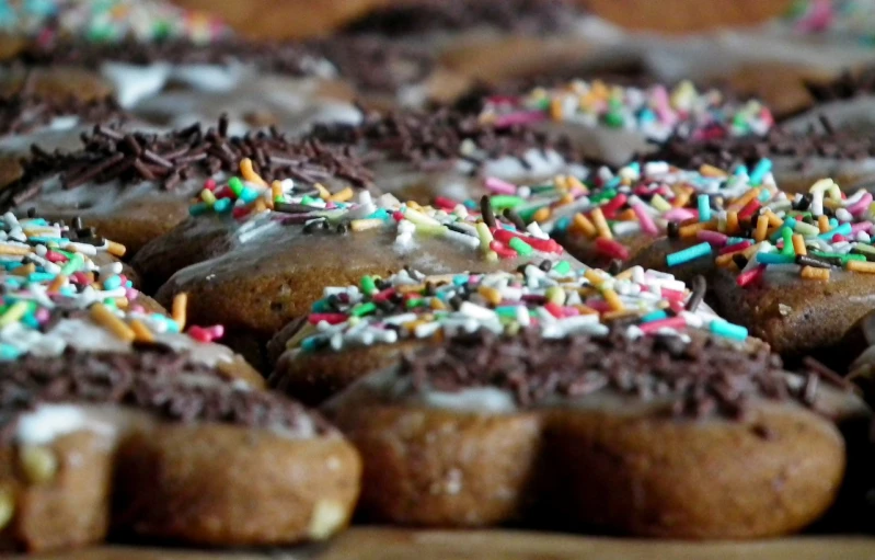 a close up of a tray of doughnuts with sprinkles, by Dietmar Damerau, flickr, hurufiyya, chocolate frosting, side - view, a wooden, sloppy