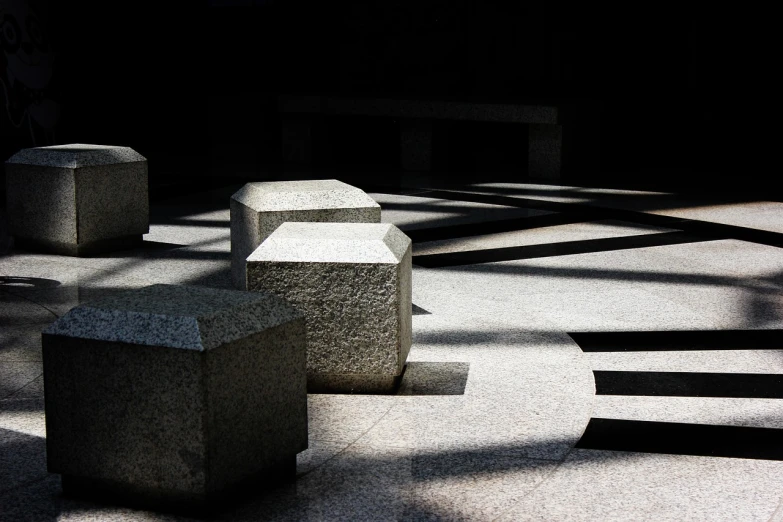 a group of concrete blocks sitting on top of a cement floor, an abstract sculpture, unsplash, light and shadow effects, tombs, terrazzo, great light and shadows”