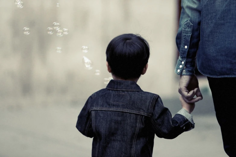 a small child holding the hand of an adult, a picture, by Jesper Knudsen, pexels, conceptual art, bubbles ”, boy has short black hair, back towards camera, asian male