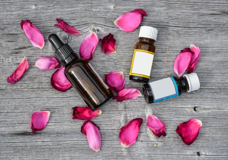 a couple of bottles sitting on top of a wooden table, a picture, shutterstock, pink petals, product photo, oils, stock photo