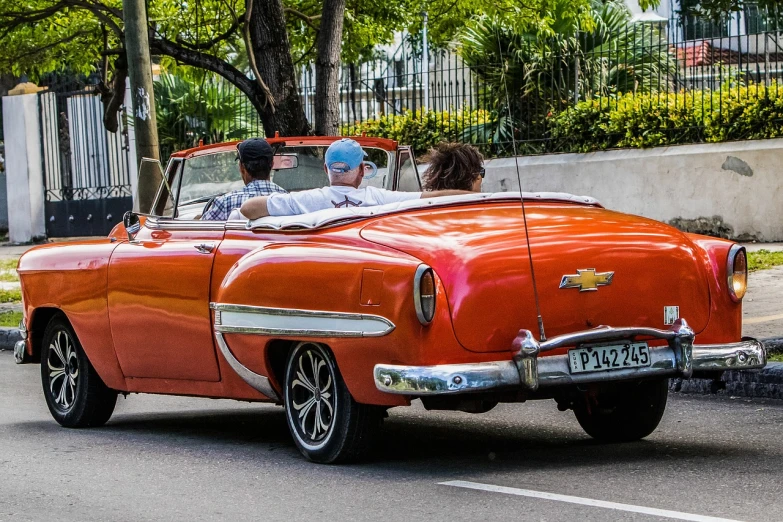 a couple of people riding in the back of a red car, pexels, pop art, cuban revolution, hdr photo, red and orange colored, soft top