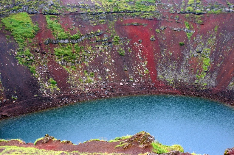 a large body of water sitting on top of a lush green hillside, a photo, by Júlíana Sveinsdóttir, color field, reddish lava highlights, partly sunken! in the lake!, balaskas, flora-lush-crater