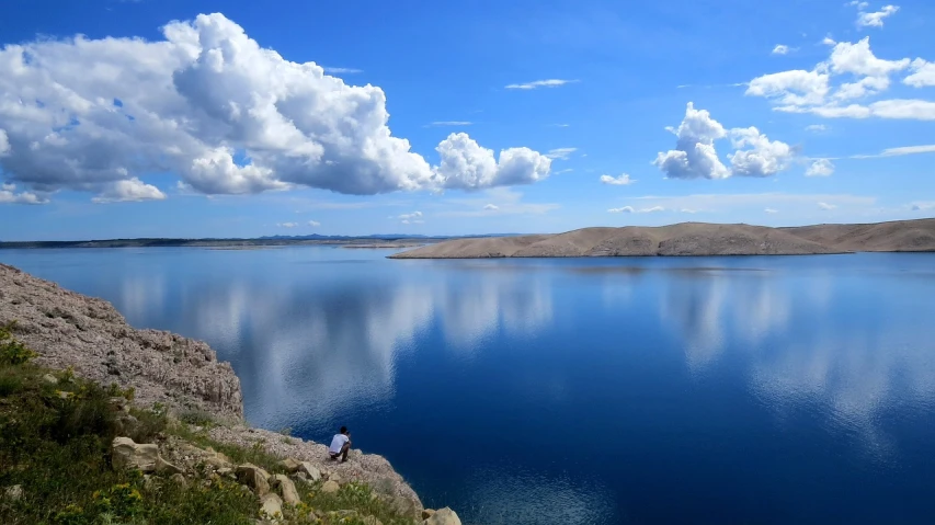 a person sitting on a rock overlooking a large body of water, by Muggur, flickr, wyoming, blue reflections, cloud, kiss