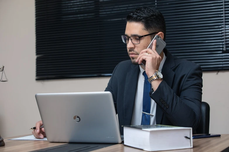 a man sitting at a desk talking on a cell phone, a stock photo, by Robbie Trevino, kurdish lawyer, working on a laptop at a desk, high resolution product photo, female lawyer