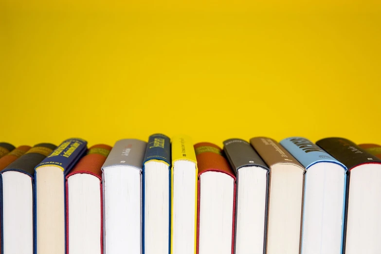 a row of books sitting on top of a table, a picture, academic art, colors: yellow, productphoto, reading a book, simplified