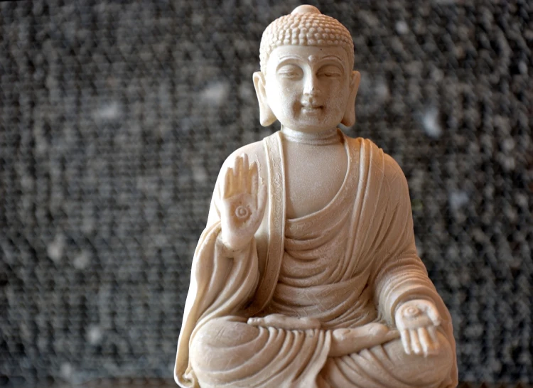 a statue of a buddha sitting on a table, a marble sculpture, figurativism, waving, small depth of field, ivory carving, anthropology photo”