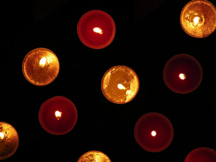 a group of lit candles sitting on top of a table, by Linda Sutton, shining gold and black and red, view from above, floating lampoons, glowing from inside