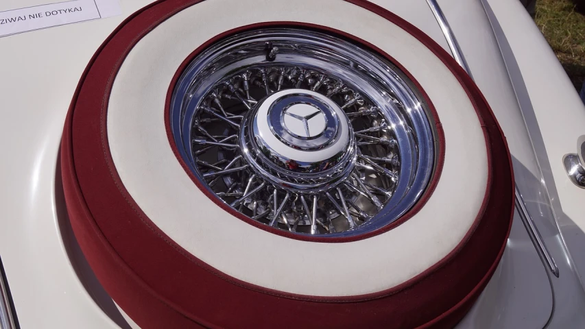 a close up of a white car with a red rim, by Bob Singer, photorealism, mercedez benz, medallion, chrome parts, ektachrome color photograph