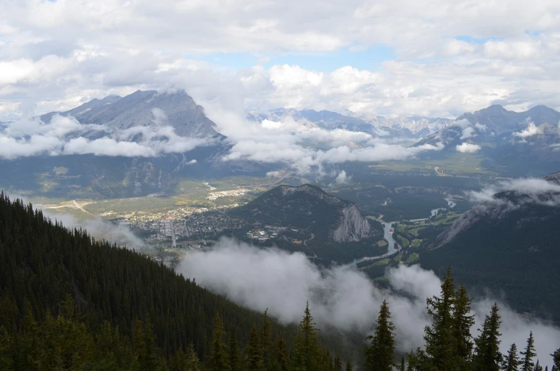 a view of a valley from the top of a mountain, by Brigette Barrager, happening, city in the clouds, banff national park, in the foreground a small town, college