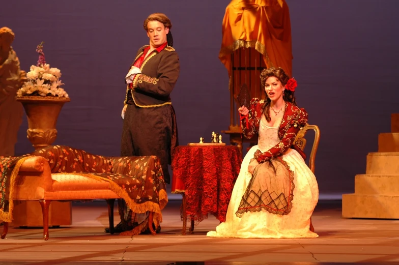 a man standing next to a woman on a stage, baroque, yellow robe, carmen sings beautifully, magazine photo from 2007, full cast