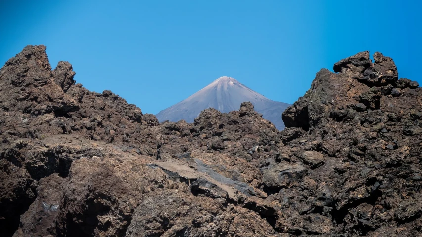 a large rock formation with a mountain in the background, a photo, by Juan O'Gorman, figuration libre, lava rock, cone, extremely clear and coherent, telephoto