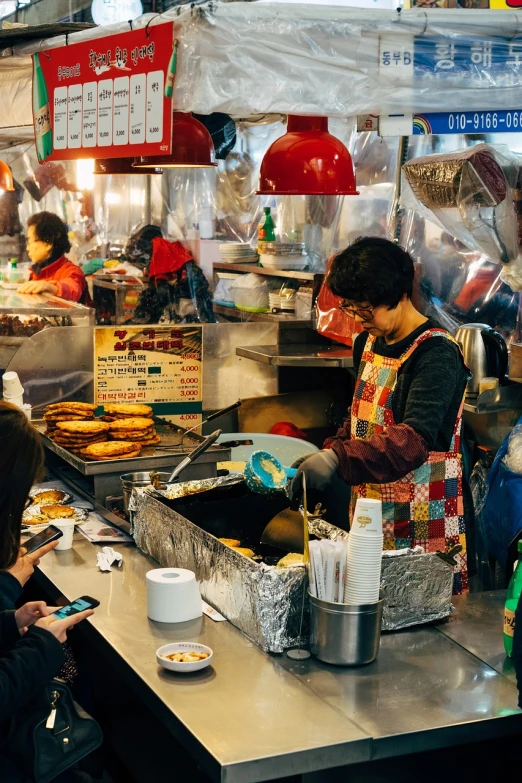 a group of people standing around a food stand, a photo, pexels, mingei, seoul, operating on burgers, 🦩🪐🐞👩🏻🦳, cooking