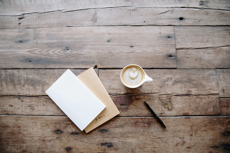 a notepad sitting on top of a wooden table next to a cup of coffee, inspired by Masamitsu Ōta, minimalism, writing a letter, milk and mocha style, creative book cover, brown and white color scheme