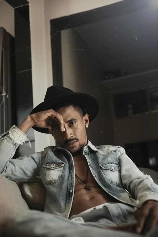 a man sitting on a couch wearing a hat, a portrait, inspired by Afewerk Tekle, pexels, sexy pose, jean deville, full protrait, promotional image