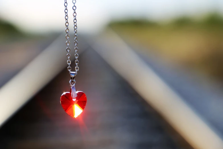 a red heart hanging from a chain on a train track, a picture, minimalism, refractive crystal jewelry, shining light, pendants, so cute