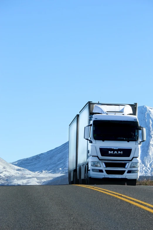 a semi truck driving down a road with a mountain in the background, a portrait, shutterstock, winter, focus on full - body, spartan, white