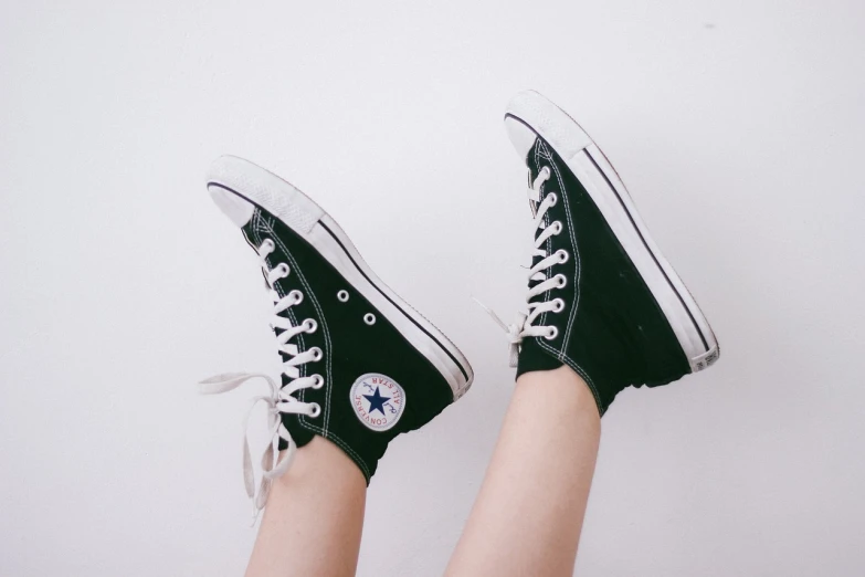 a pair of black converse sneakers with white laces, tumblr, visual art, mid view from below her feet, green and black colors, on a white table, aaaaaaaaaaaaaaaaaaaaaa
