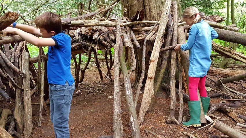 a couple of kids standing next to each other in a forest, inspired by Patrick Dougherty, flickr, land art, witch hut, 🕹️ 😎 🔫 🤖 🚬, huge level structure, cedar