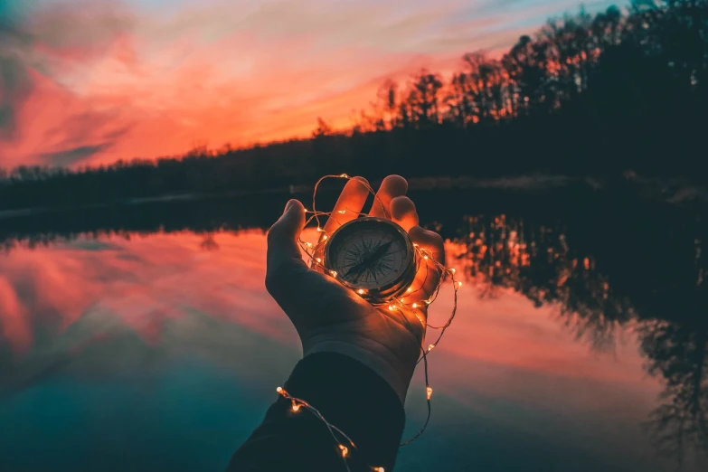 a person holding a clock in front of a lake, romanticism, colorful light, close up shot of an amulet, orange lights, connections