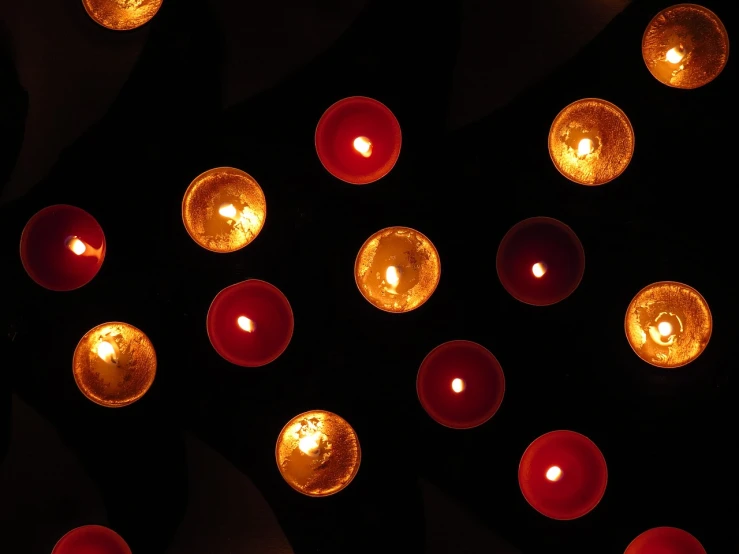 a group of lit candles sitting on top of a table, by David Garner, pexels, light and space, shining gold and black and red, view from above, lights on ceiling, circles