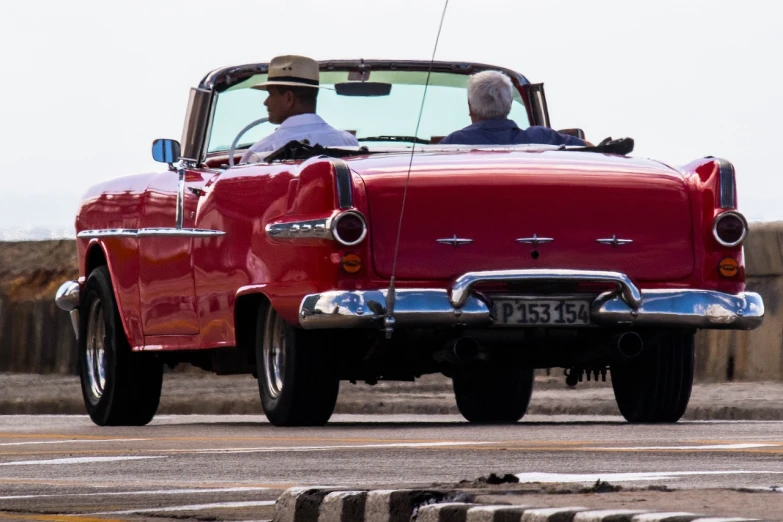 a man driving a red classic car down a street, varadero beach, 15081959 21121991 01012000 4k, square, back turned