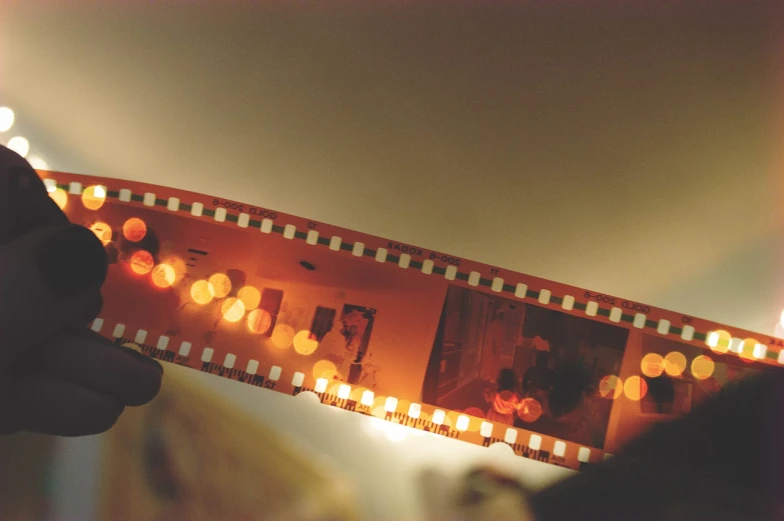 a close up of a person holding a film strip, by Pamela Ascherson, unsplash, serial art, orange lights, 5 0 mm 1 9 4 6 historical photo, 1 9 7 0 s film, cinematic view from lower angle