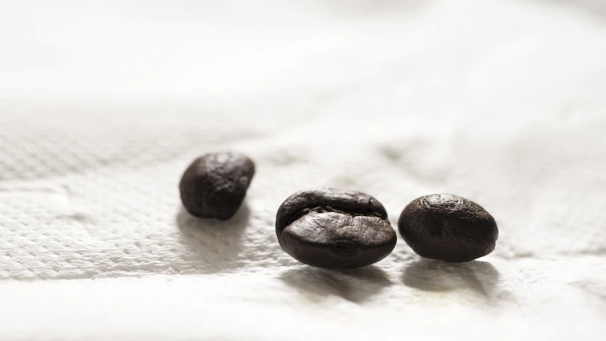 three black olives sitting on top of a white cloth, a macro photograph, portrait of morning coffee, high res photo