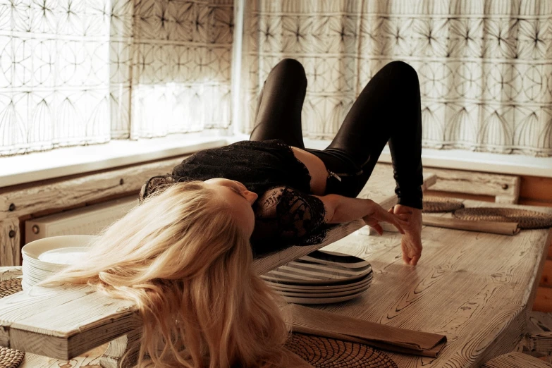 a woman laying on top of a wooden table, a picture, by Zofia Stryjenska, tumblr, arabesque, black canary, in a kitchen, desperate pose, blonde women