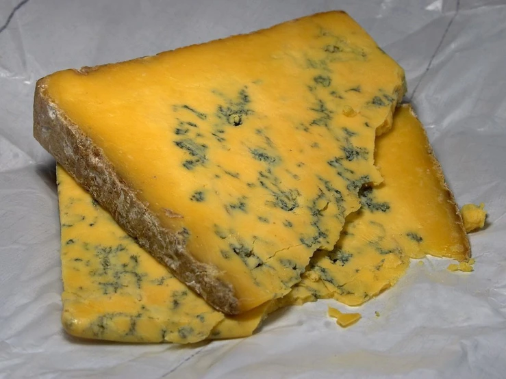 a piece of cheese sitting on top of a piece of paper, by Julian Hatton, reddit, hurufiyya, blue skin, britain, from wikipedia, beautiful black blue yellow