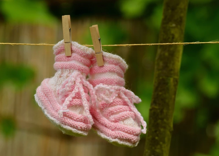 a pair of baby shoes hanging on a clothes line, a photo, figuration libre, pink, close - up photo, outdoor photo, socks