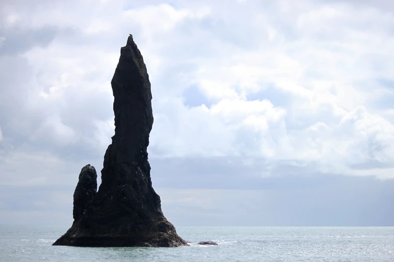 a large rock formation in the middle of the ocean, inspired by Þórarinn B. Þorláksson, spire, photo from the side, a creature 5 meters tall, wikimedia