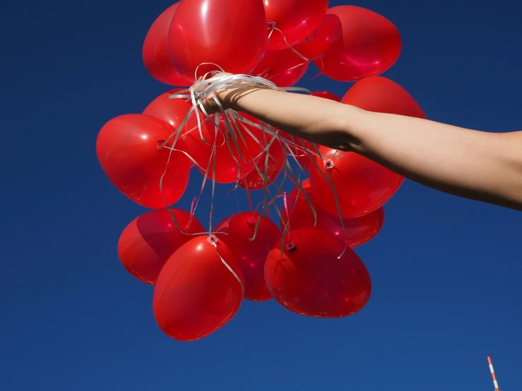 a person holding a bunch of red balloons, by Andrei Kolkoutine, happening, vertical wallpaper, closeup of arms, blue sky, hila klein