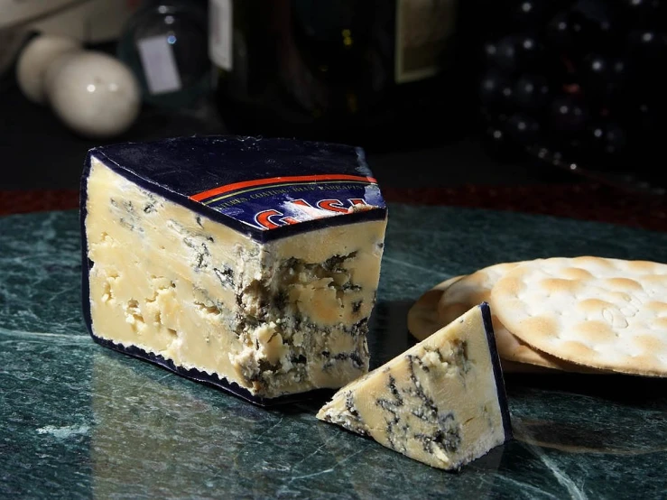 a piece of cheese sitting on top of a table next to crackers, a portrait, by Doug Ohlson, renaissance, blue and black color scheme, chesterfield, gooey skin, deep blue