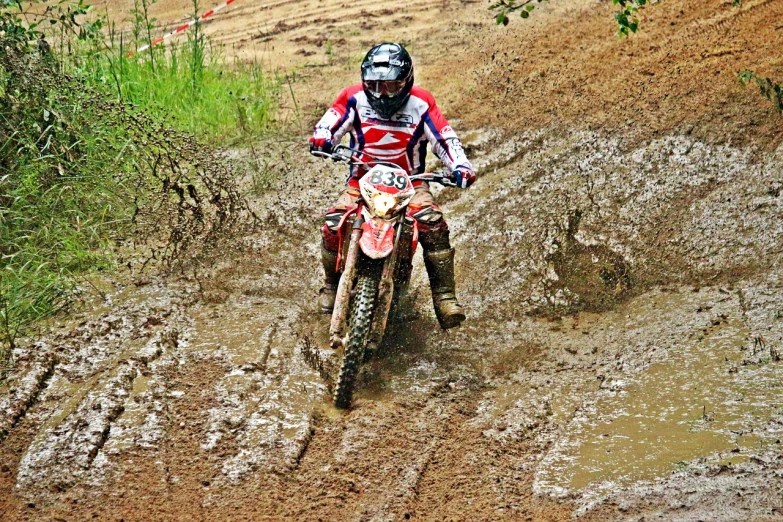 a man riding a dirt bike on a muddy road, a photo, flickr, figuration libre, rain!!!!, mateus 9 5, red shell. dirt track, muddy embankment