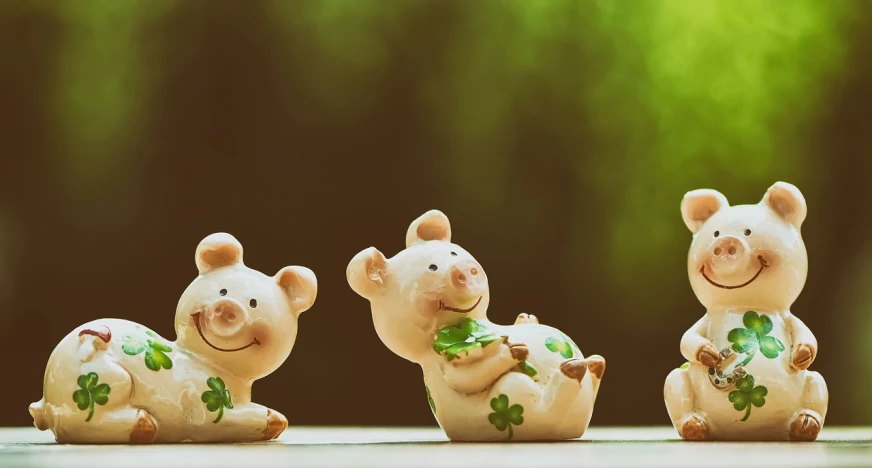 three ceramic pig figurines sitting next to each other, a picture, by Adam Marczyński, trending on pixabay, background full of lucky clovers, tan, pvc figurine, banner