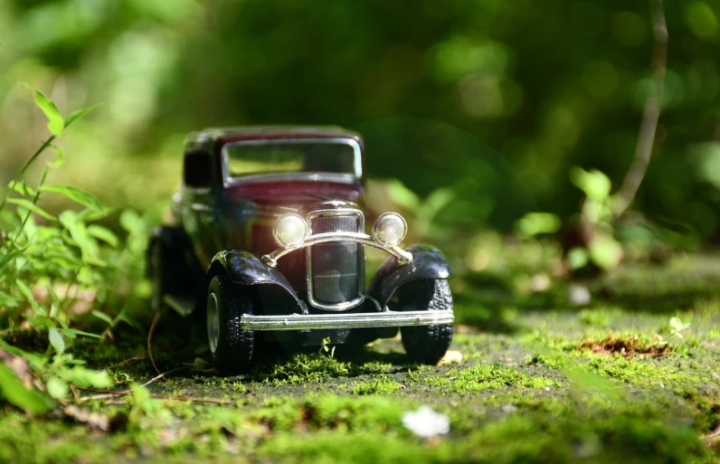 a toy car sitting on top of a lush green field, a tilt shift photo, inspired by Otto Eckmann, photorealism, car lights, mobile wallpaper, in picturesque forest diorama, vintage - w 1 0 2 4