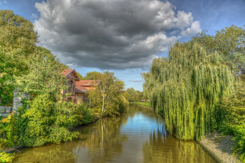 a river running through a lush green forest filled with trees, by Karl Hagedorn, flickr, modernism, dutch houses along a river, weeping willows, hdr photo, brooding clouds'