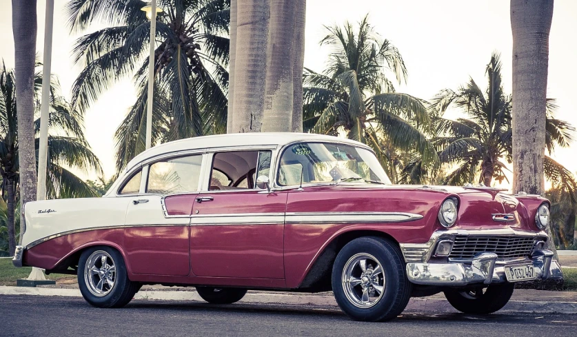 a red and white car parked on the side of the road, a colorized photo, by Reuben Nakian, pexels, varadero beach, brown and magenta color scheme, looking regal and classic, lit from the side