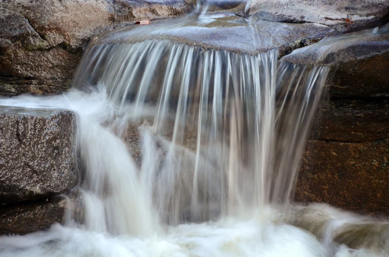 a close up of a waterfall with rocks in the background, a picture, by Tom Carapic, flash photo, water particules, realistic water, motivational