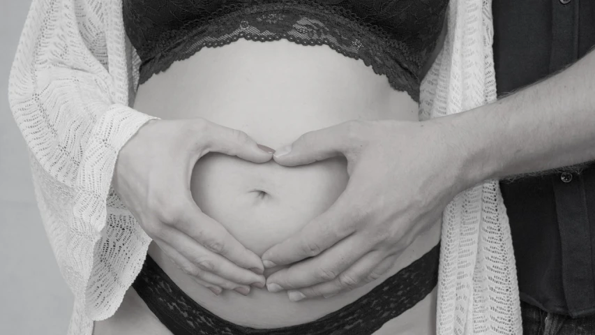 a pregnant woman making a heart shape with her hands, a black and white photo, by Matija Jama, pixabay, digital art, belly button showing, photorealistic detail, diaper-shaped, banner