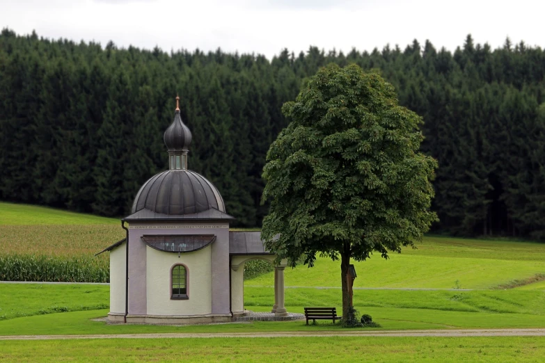 a small church sitting on top of a lush green field, a picture, inspired by Georg Friedrich Schmidt, baroque, mausoleum, forest in the background, tourist photo, july 2 0 1 1