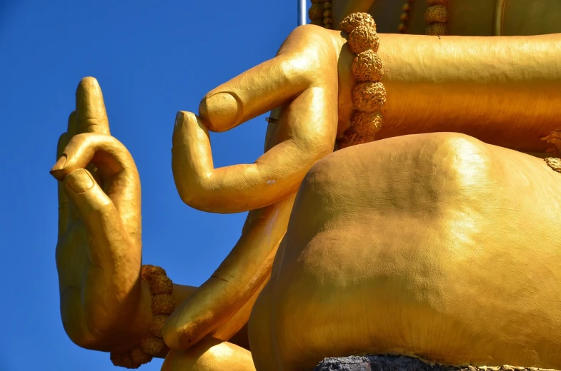 a close up of a gold statue with a blue sky in the background, a statue, minimalism, fisting monk, colourful biomorphic temple, high detail of a hand, huge statues