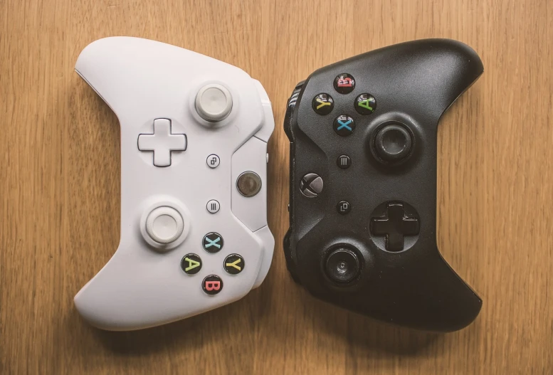 a couple of controllers sitting on top of a wooden table, a picture, 4 k product photo, microsoft, one contrasting small feature, black an white