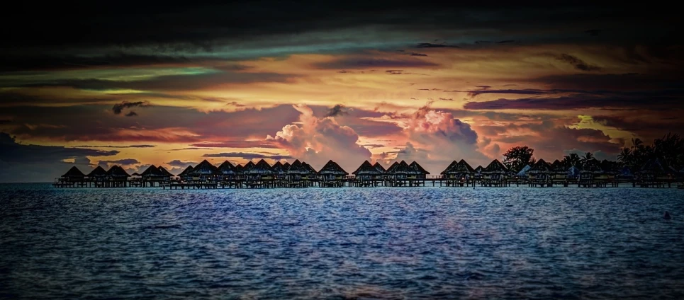 a group of huts sitting on top of a body of water, a portrait, by Erik Pevernagie, flickr, sunset with cloudy skies, polynesian style, color corrected, 💋 💄 👠 👗
