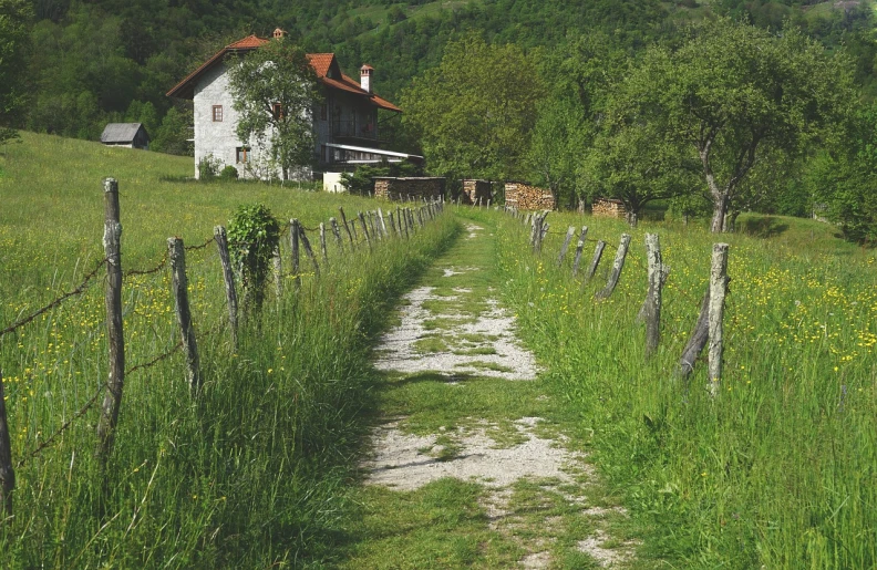 a white house sitting on top of a lush green hillside, a picture, inspired by Hristofor Žefarović, ((((dirt brick road)))), slovenian, rustic setting, walking towards the camera