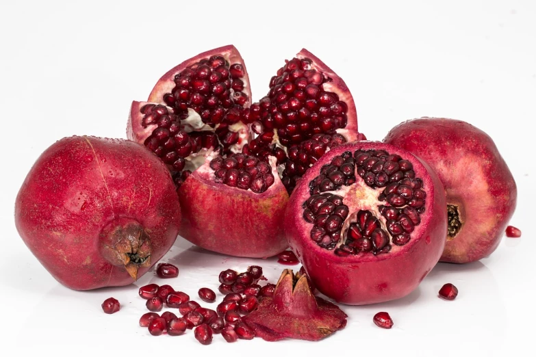 a group of pomegranates on a white surface, a still life, by Johannes van Haensbergen, pixabay, 🦩🪐🐞👩🏻🦳, opening shot, food particles, compressed jpeg