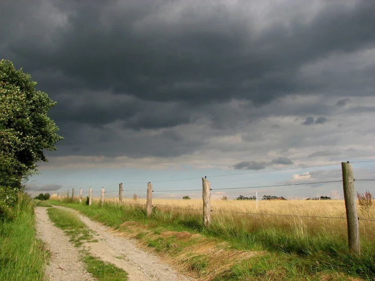 a dirt road next to a fence on a cloudy day, a picture, by Karl Pümpin, flickr, big storm clouds, in summer, looking left, sturm und drang