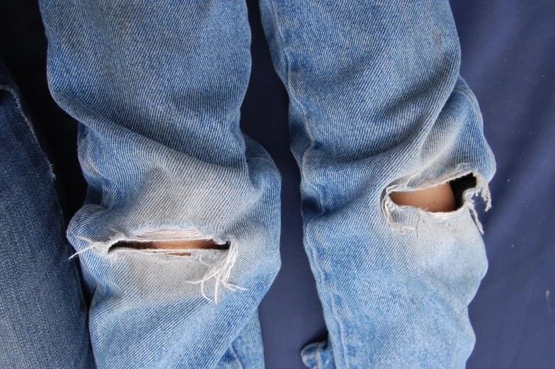 a pair of ripped jeans sitting on top of a bed, pexels, detail, panel, holes, istockphoto