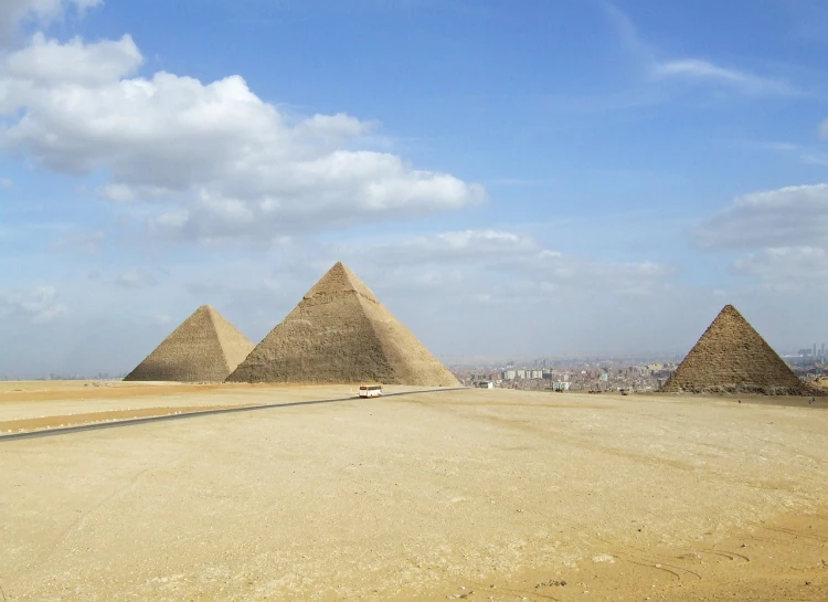 a group of three pyramids sitting in the middle of a desert, egyptian art, in a city with a rich history, sweeping vista, blue sky, wikimedia